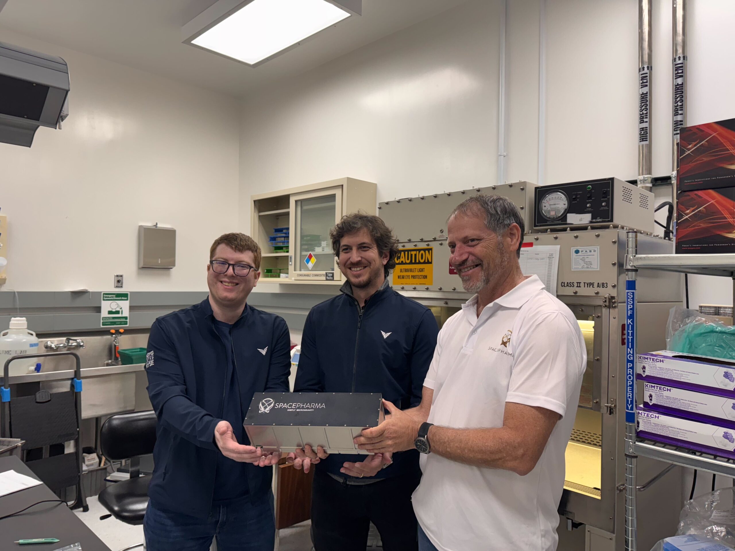 Three scientists smiling in lab holding SpacePharma equipment