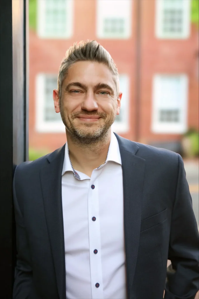 Man in suit smiling against brick building backdrop