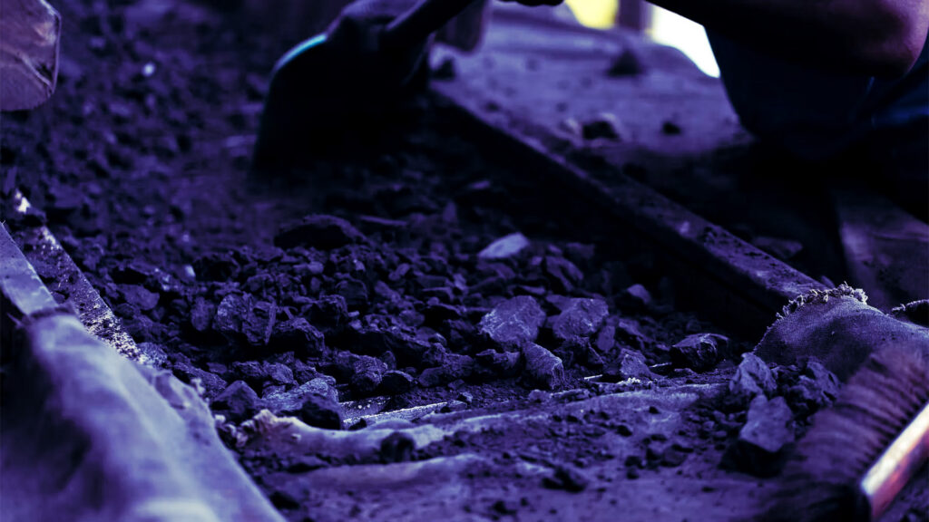 Gloved worker sorting dark ore fragments in a tray