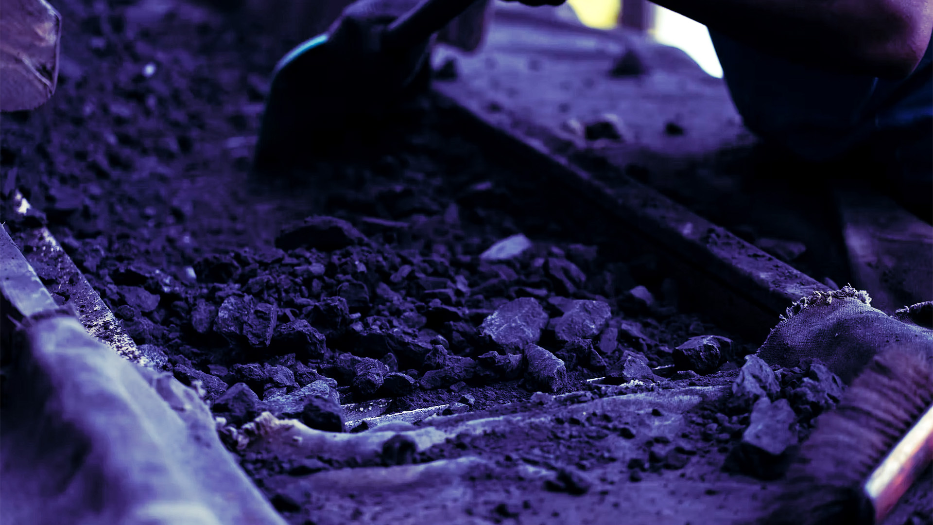 Gloved worker sorting dark ore fragments in a tray